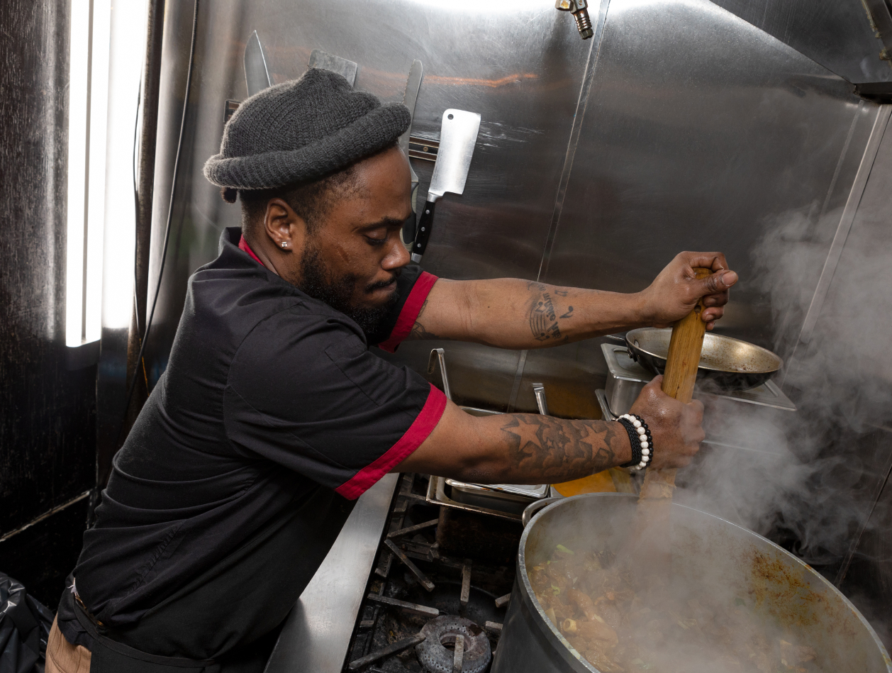 Kemar stirs a large pot of slow-cooked oxtail.